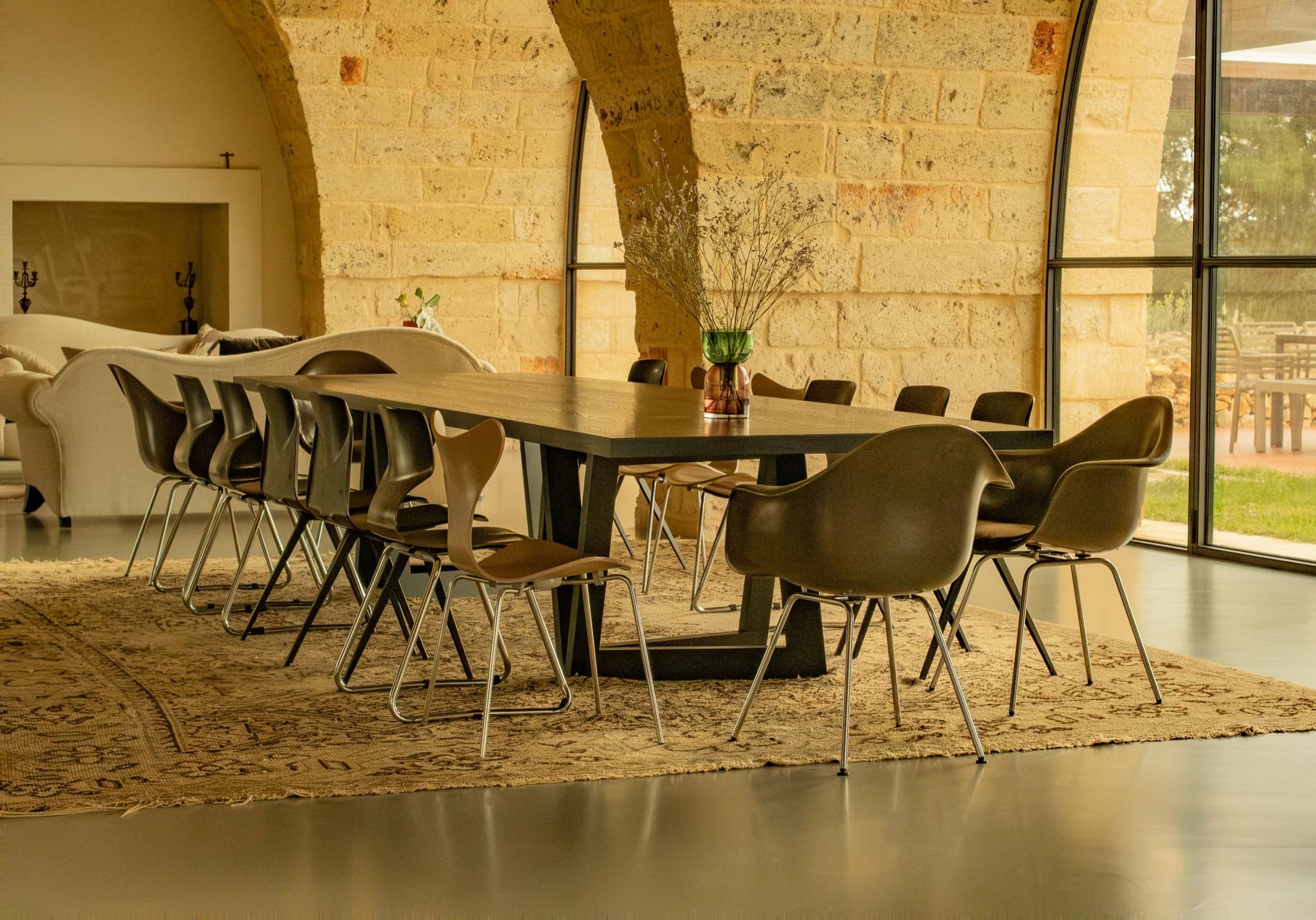 A long dining table set under a stone vault, with glass walls opening onto the garden