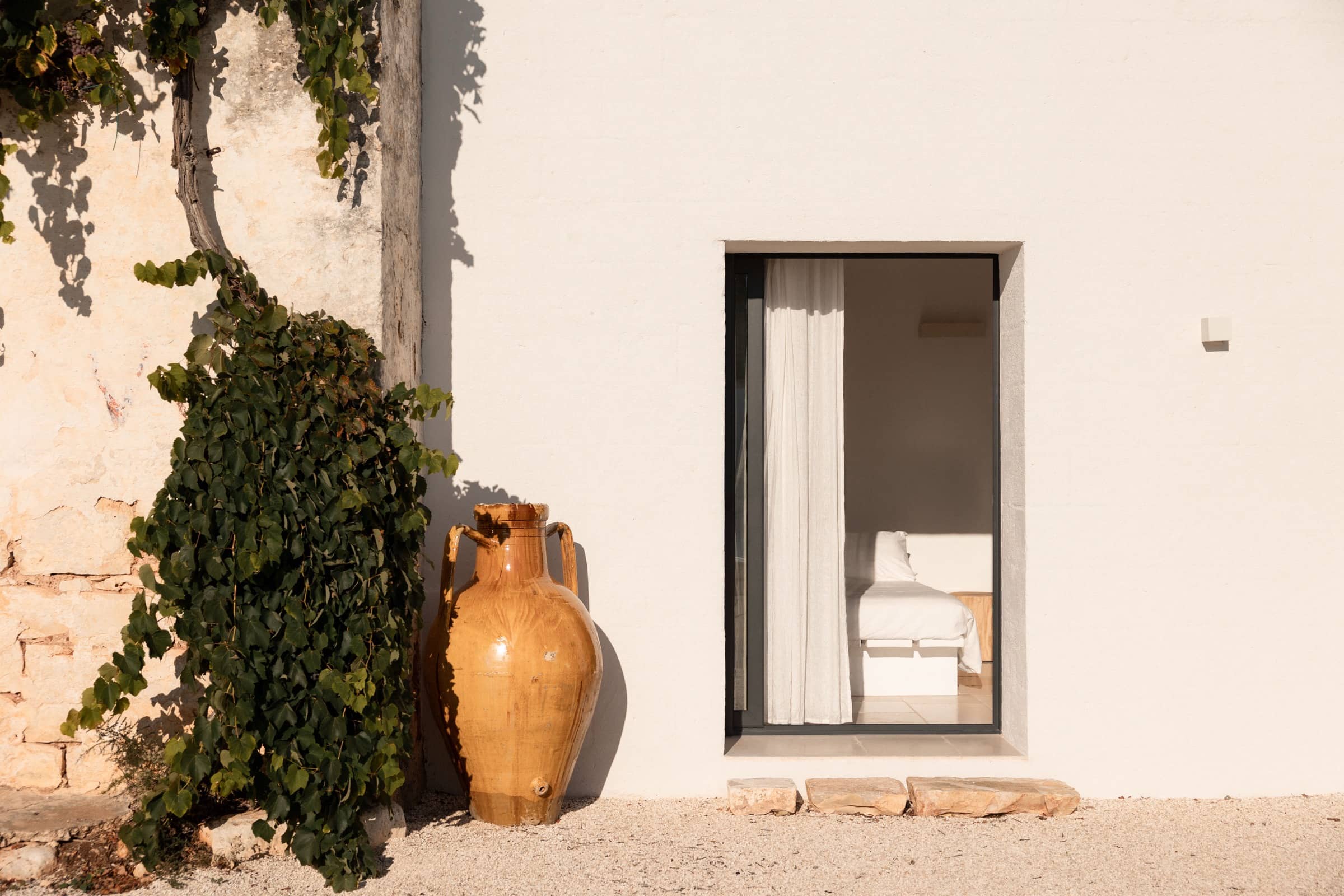 A whitewashed masseria wall with a terracotta amphora and a curtained doorway, near Ostuni